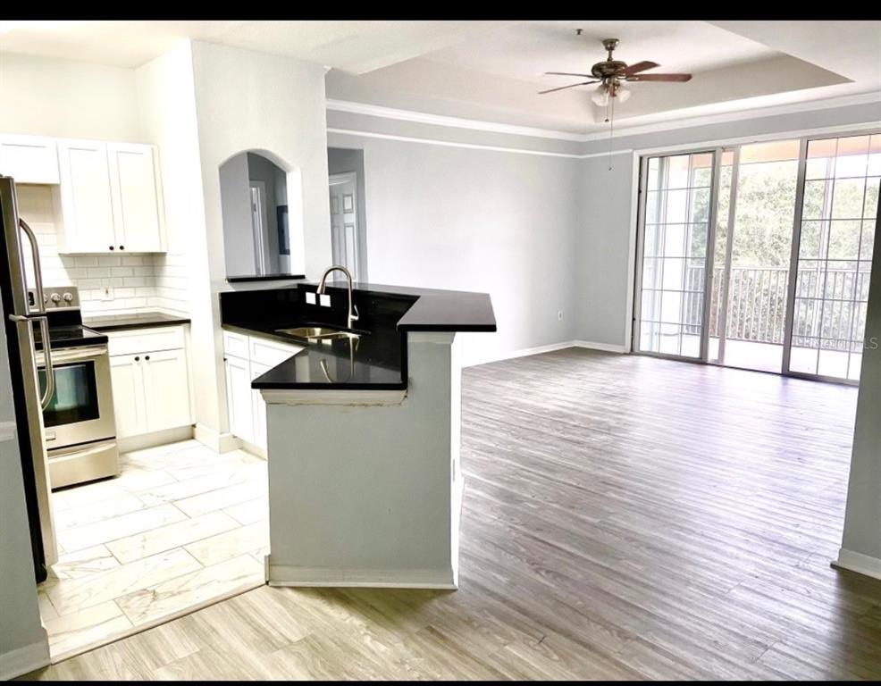 A kitchen with white cabinets and black countertops opens to a living area with wood flooring — 6412 QUEENS BOROUGH AVENUE UNIT 315, ORLANDO, FL