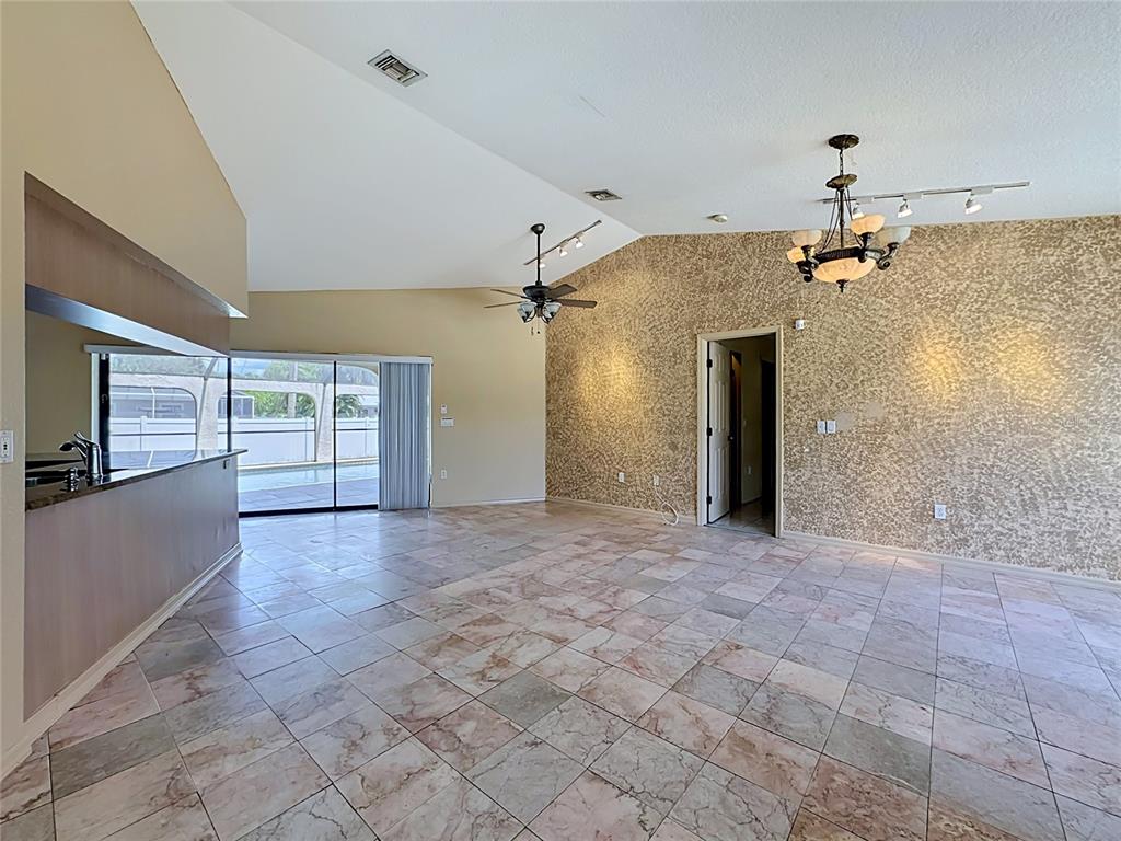 A living room with vaulted ceilings, tiled floors, a textured accent wall, and sliding glass doors — 4354 BOGGS STREET, PORT CHARLOTTE, FL