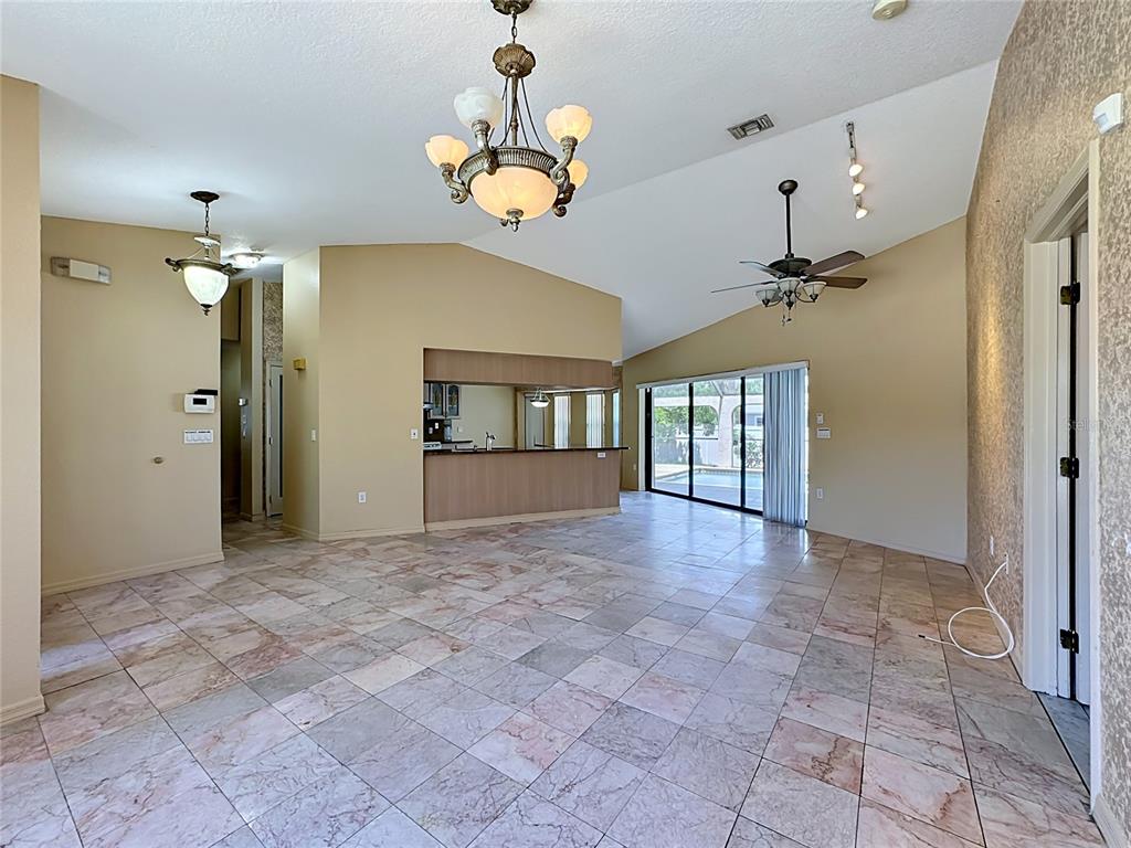 A living room with vaulted ceilings, tile flooring, a chandelier, and a kitchen pass-through window — 4354 BOGGS STREET, PORT CHARLOTTE, FL