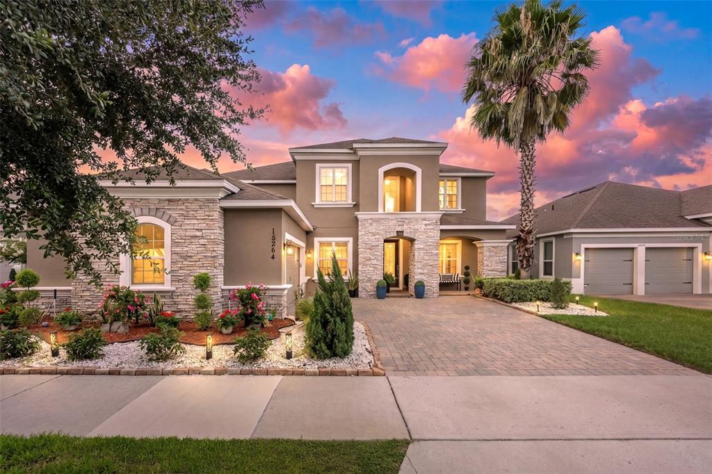A two-story house with a stone facade, arched entryway, and a paved driveway at sunset — 15264 SHONAN GOLD DRIVE, WINTER GARDEN, FL