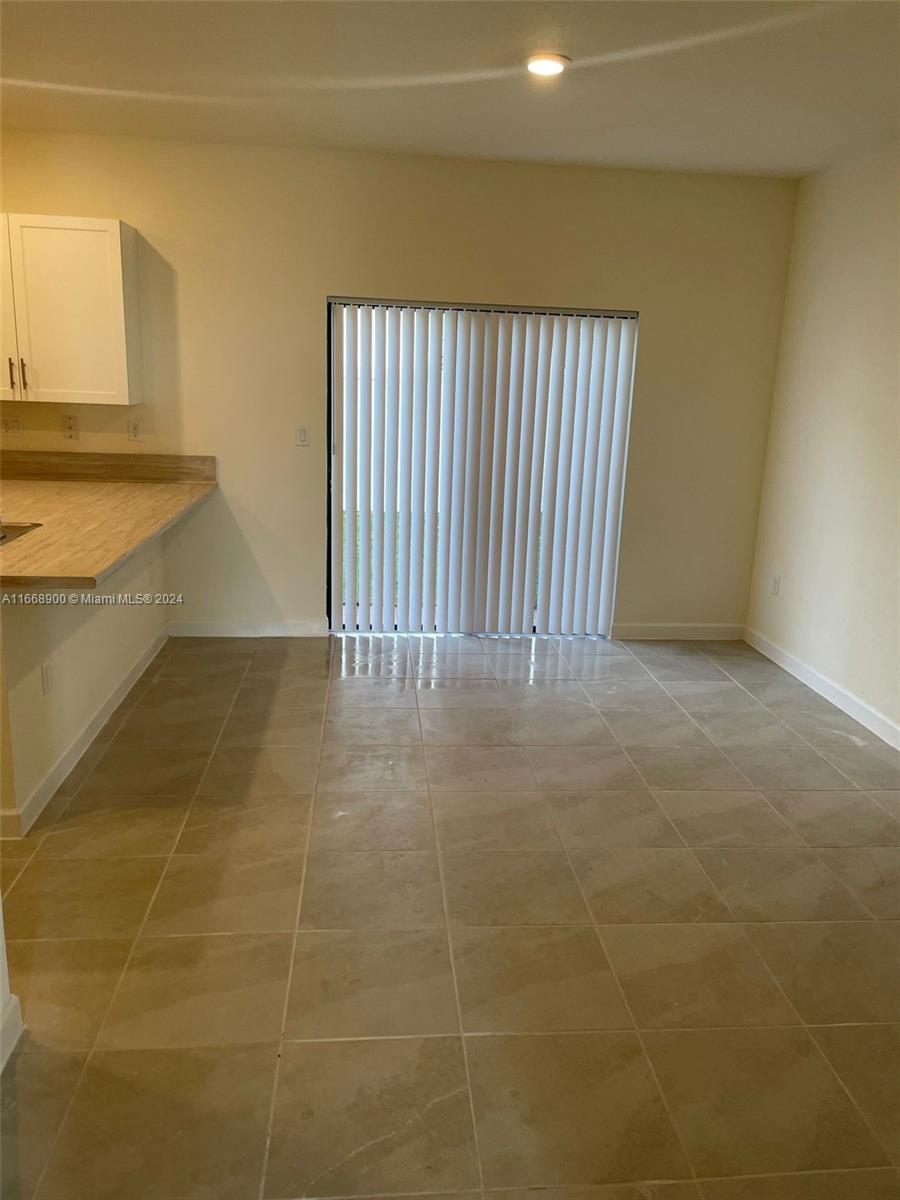 A kitchen area with light-colored cabinets, a wood-look countertop, and a sliding glass door — 3415 W 112th Ter, Hialeah FL 33018, HIALEAH, FL