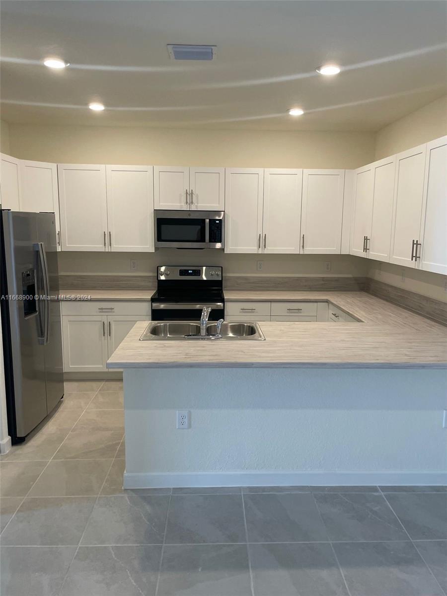 A kitchen features white cabinets, stainless steel appliances, and a light-colored wood-look countertop — 3415 W 112th Ter, Hialeah FL 33018, HIALEAH, FL