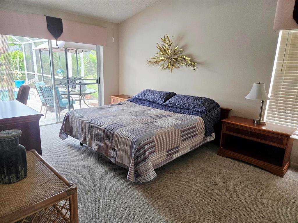 A bedroom features a bed with a patterned quilt, wooden nightstands, and a sliding glass door — 4236 PRO AM AVE E, BRADENTON, FL