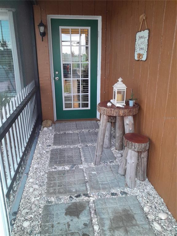 A covered porch features a green door, stone pavers, and rustic log-style furniture — 6417 KLAUS COURT, PORT CHARLOTTE, FL