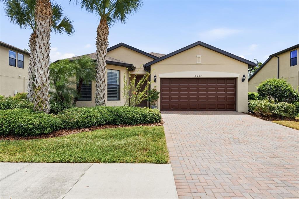 A single-story house with a brown garage door, tan stucco walls, and two palm trees — 2501 SHERMAN OAK DRIVE, NORTH PORT, FL