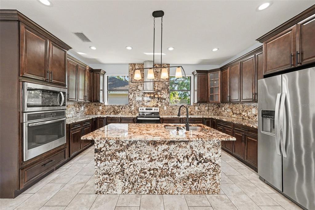 A kitchen with dark wood cabinets, granite countertops, a central island, and stainless steel appliances — 7110 N TALIAFERRO AVENUE, TAMPA, FL