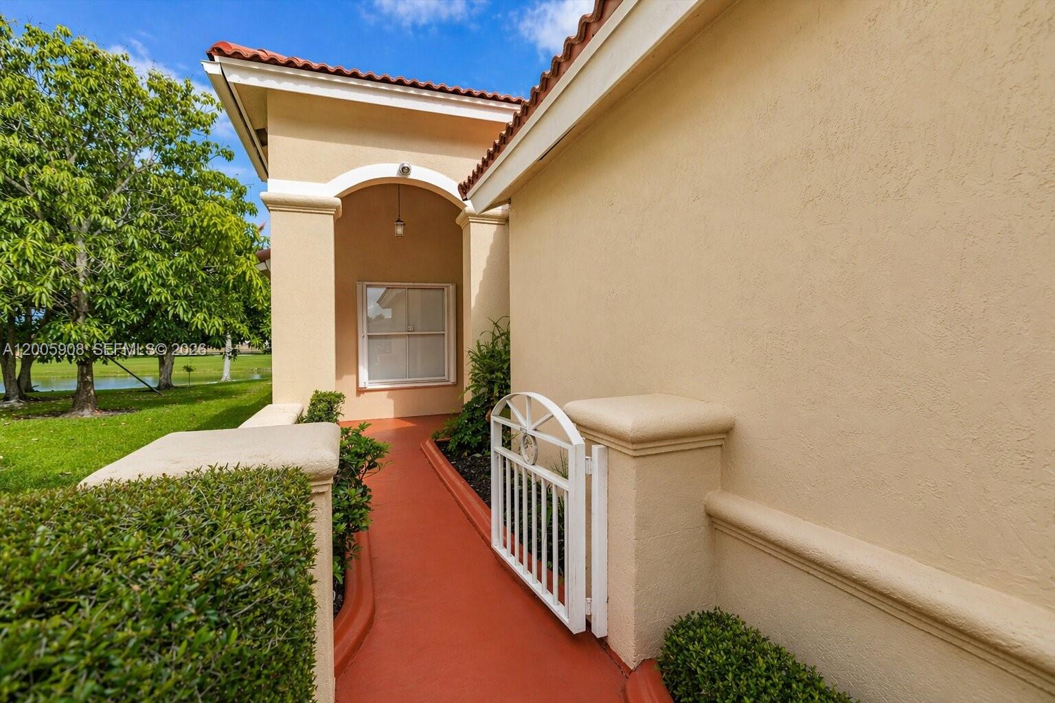A red walkway leads to a white gate beside a tan stucco house exterior — 6298 Harbour Chase Dr, Lake Worth FL 33467, LAKE WORTH, FL
