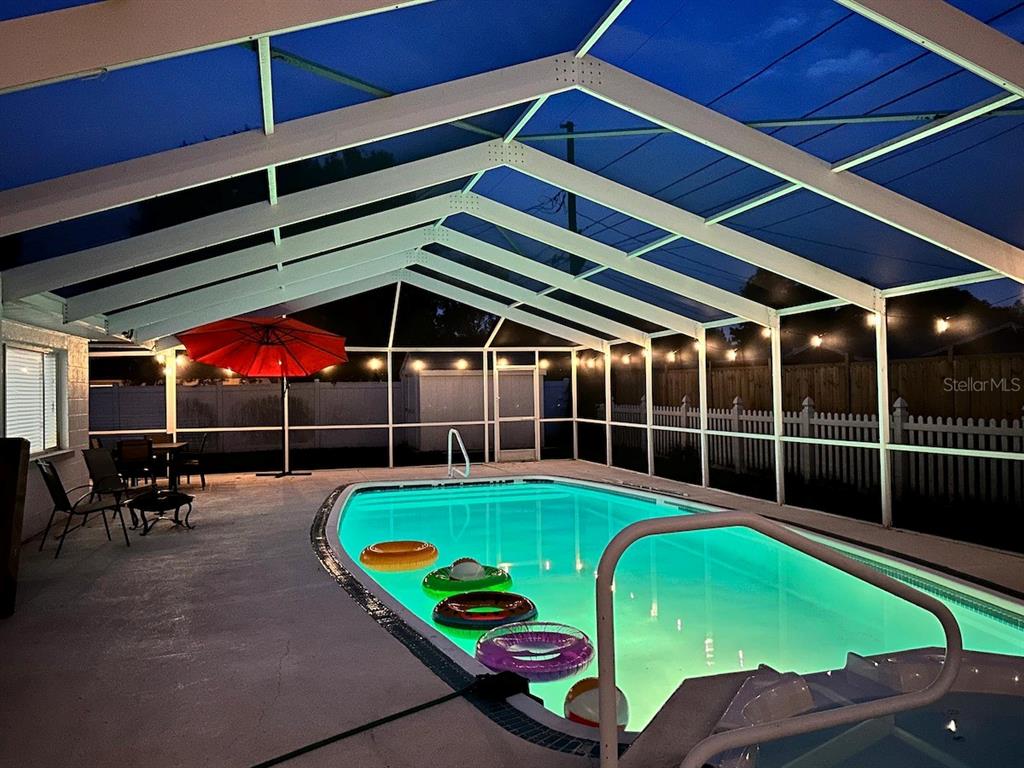 A screened-in swimming pool at night with floating rings and a red patio umbrella — 8628 MAGNOLIA DRIVE, SEMINOLE, FL