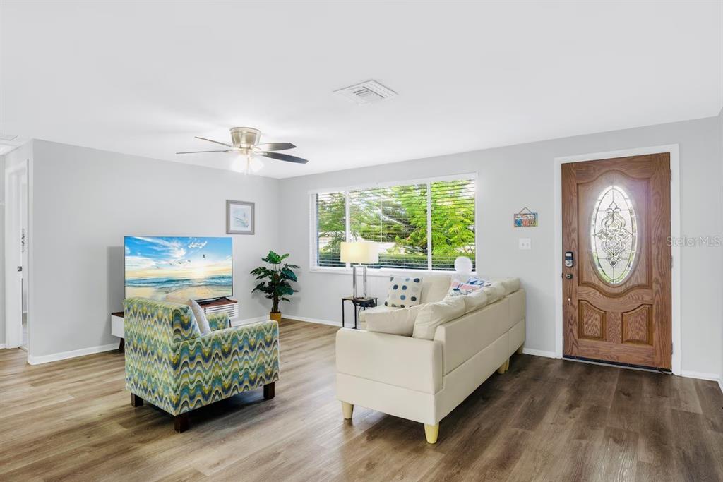 A living room features light wood-look flooring, a white sofa, a patterned armchair, and a television — 8628 MAGNOLIA DRIVE, SEMINOLE, FL