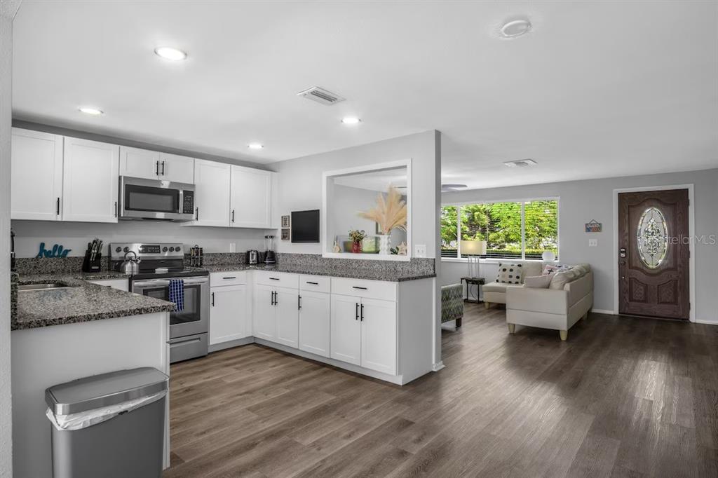 A kitchen with white cabinets and granite countertops opens into a living room with wood floors — 8628 MAGNOLIA DRIVE, SEMINOLE, FL