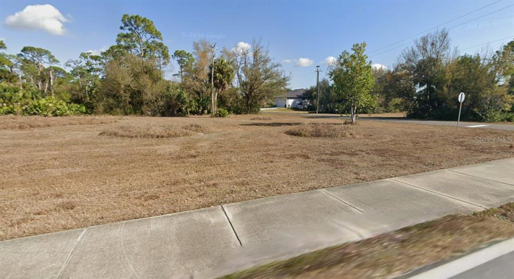 A vacant, grassy residential lot features a sidewalk in the foreground and surrounding trees — 16582 CAPE HORN BOULEVARD, PUNTA GORDA, FL