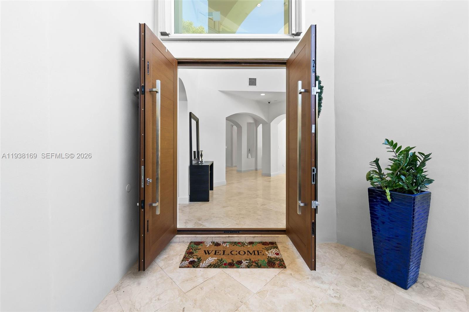 A pair of wooden front doors opens into a bright, tiled entryway with arched hallways — 1490 Cleveland Rd, Miami Beach FL 33141, MIAMI BEACH, FL