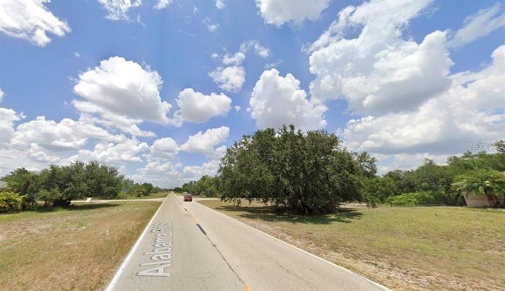 A paved road stretches into the distance under a bright blue sky with scattered clouds — 1088 ALABAMA ROAD S, LEHIGH ACRES, FL