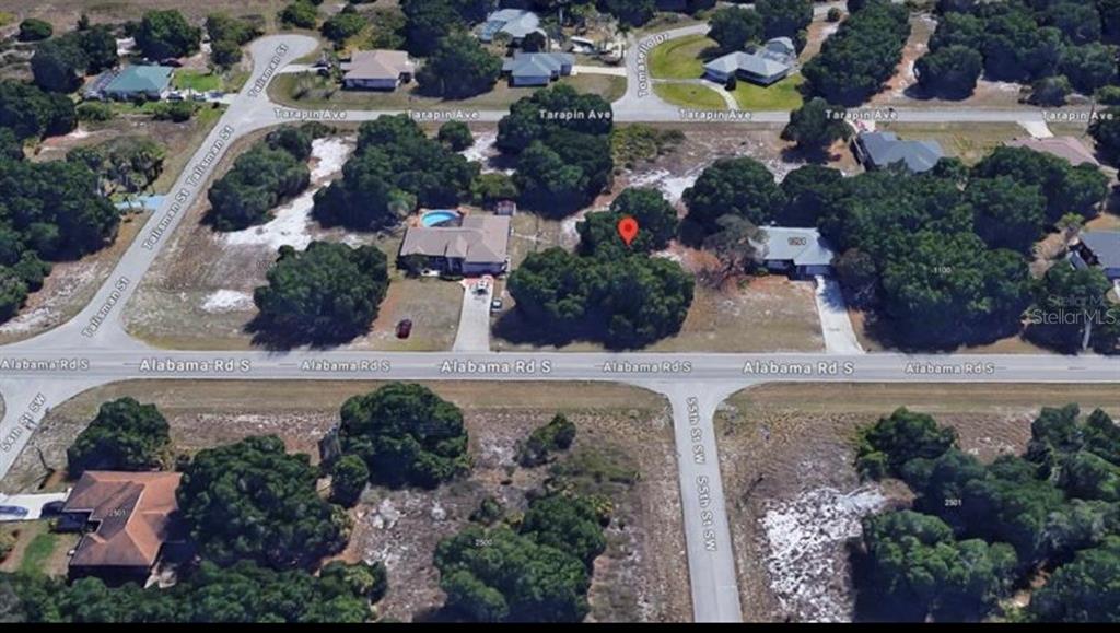 An aerial view shows a vacant, wooded residential lot situated between two houses on a street — 1088 ALABAMA ROAD S, LEHIGH ACRES, FL