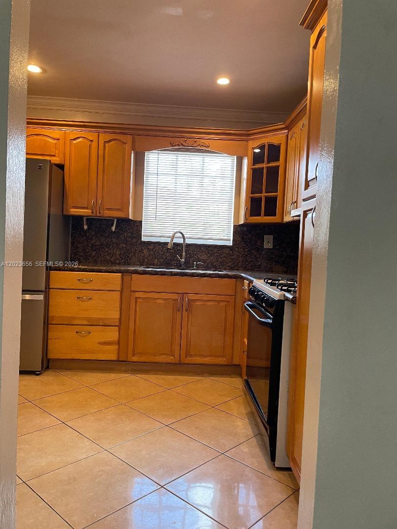 This kitchen features honey-toned wooden cabinets, dark granite countertops, and light-colored diagonal floor tiles — 1225 NW 189th Ter, Miami Gardens FL 33169, MIAMI GARDENS, FL