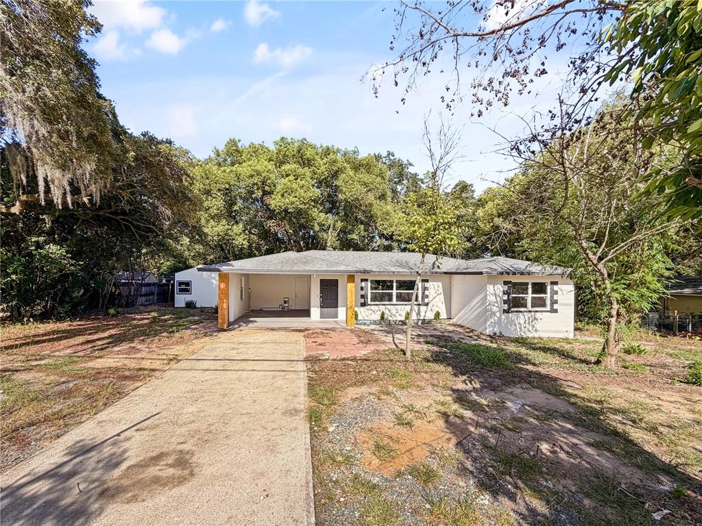 A single-story house with a white exterior, a carport, and a concrete driveway — 14418 S GRAND HIGHWAY, CLERMONT, FL
