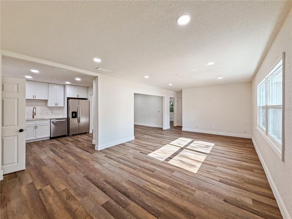An open-concept living area with wood-look flooring connects to a kitchen featuring white cabinets — 14418 S GRAND HIGHWAY, CLERMONT, FL