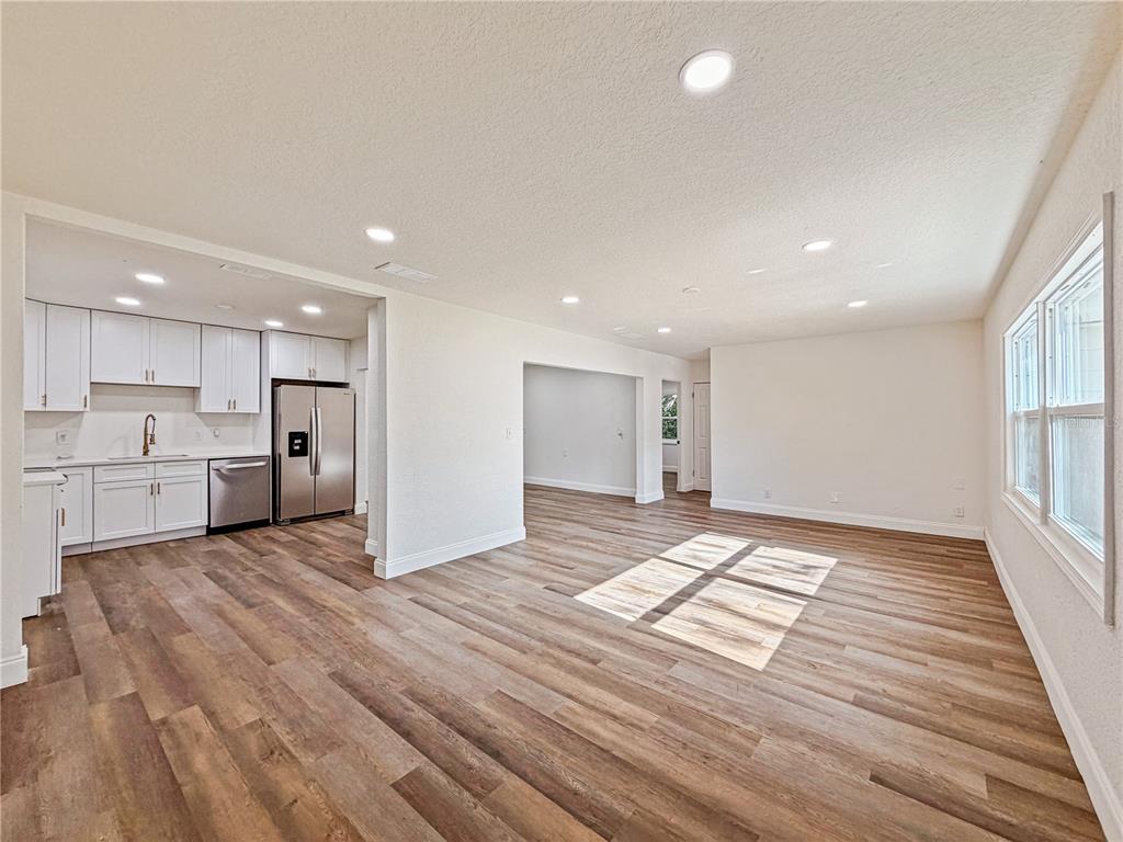 A kitchen with white cabinets and stainless steel appliances opens into a spacious living area — 14418 S GRAND HIGHWAY, CLERMONT, FL