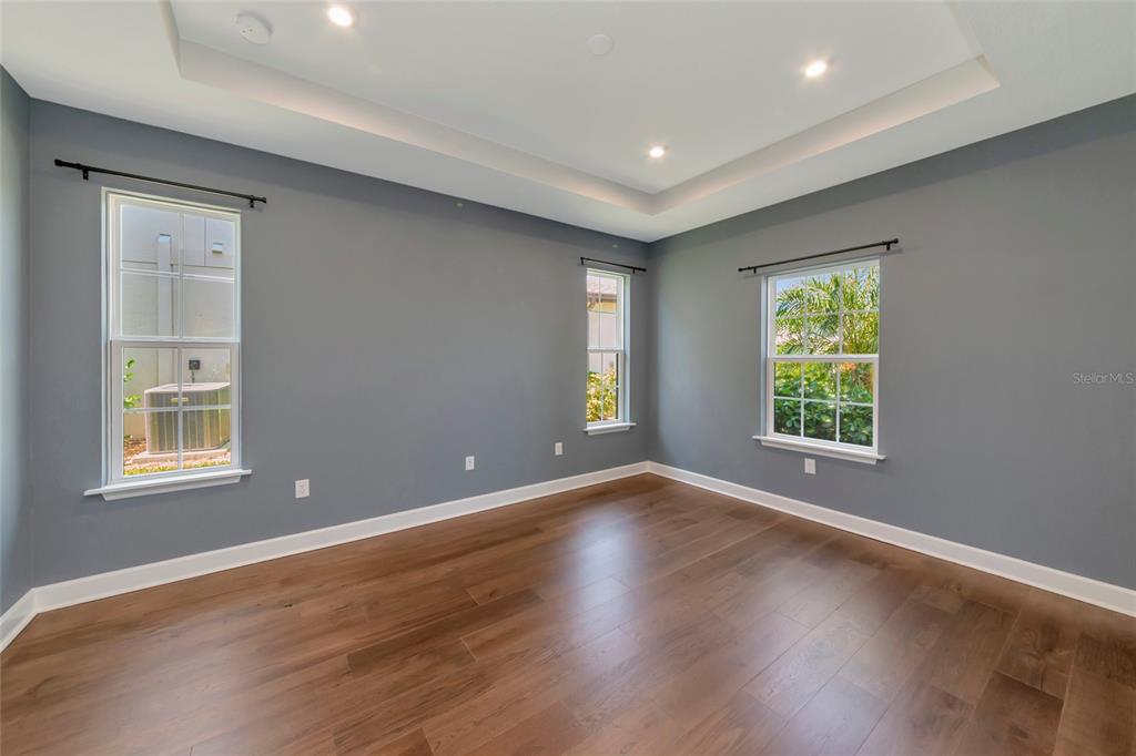An empty room with gray walls, wood flooring, a tray ceiling, and three windows — 10187 MILKY WAY CIRCLE, SARASOTA, FL