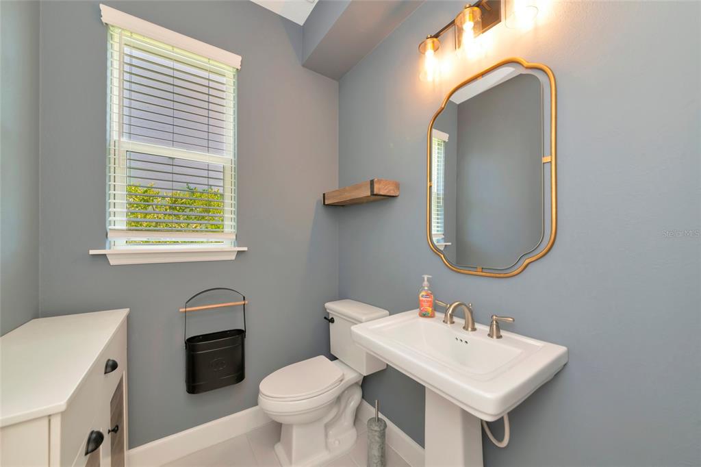 A powder room features blue walls, a pedestal sink, a gold-framed mirror, and a toilet — 10187 MILKY WAY CIRCLE, SARASOTA, FL