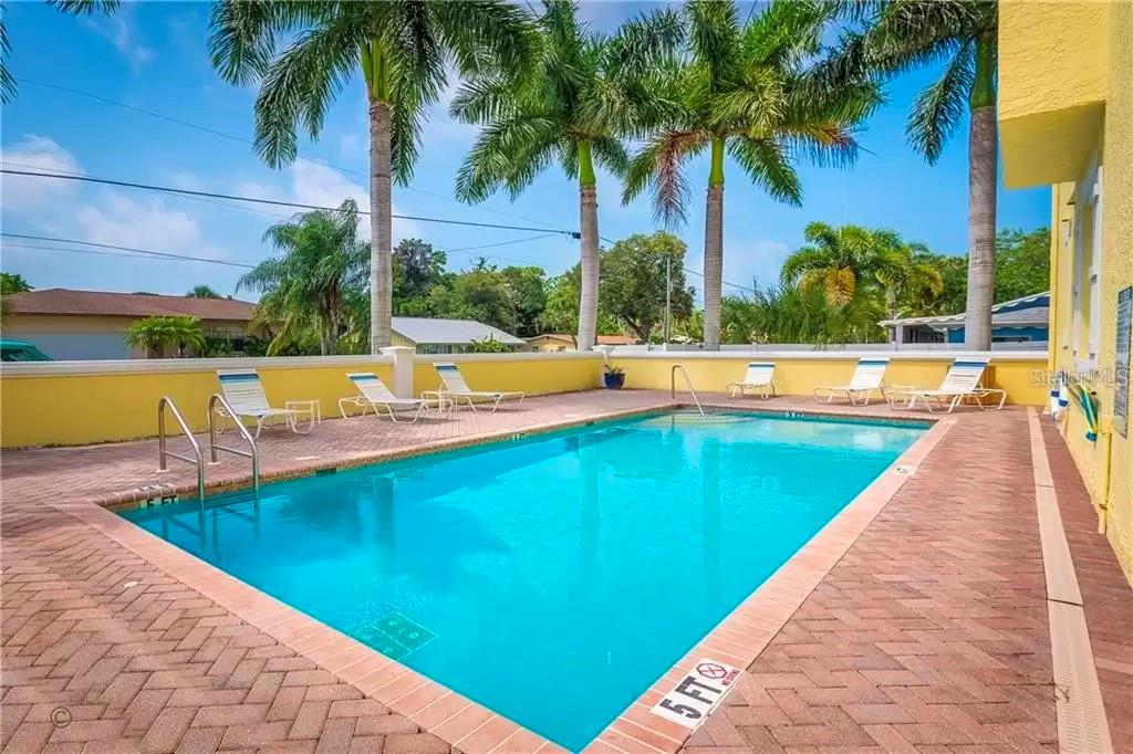 A rectangular swimming pool with a brick deck and lounge chairs under palm trees — 8920 DUVAL LANE UNIT B15, SARASOTA, FL
