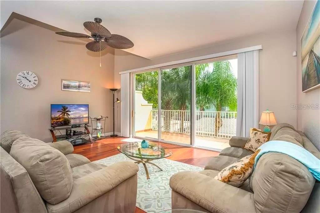 A living room features a ceiling fan, hardwood floors, a glass coffee table, and sliding doors — 8920 DUVAL LANE UNIT B15, SARASOTA, FL