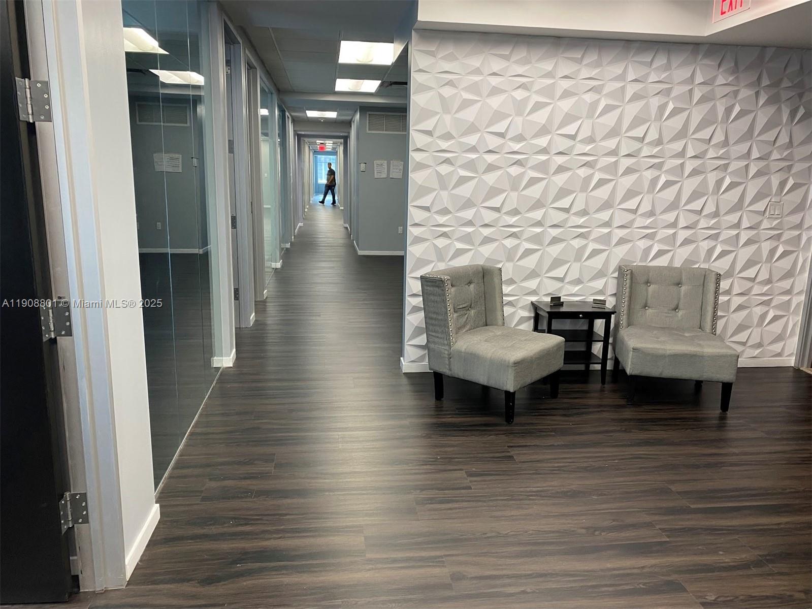 A hallway with dark wood flooring features a textured white wall and two gray chairs — 14 NE 1st Ave # 600A, Miami FL 33132, MIAMI, FL