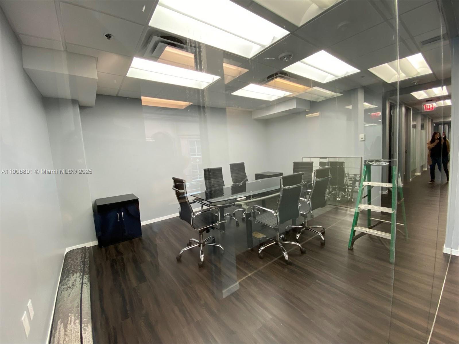A modern glass-walled conference room features a dark table, rolling chairs, and wood-look flooring — 14 NE 1st Ave # 600A, Miami FL 33132, MIAMI, FL