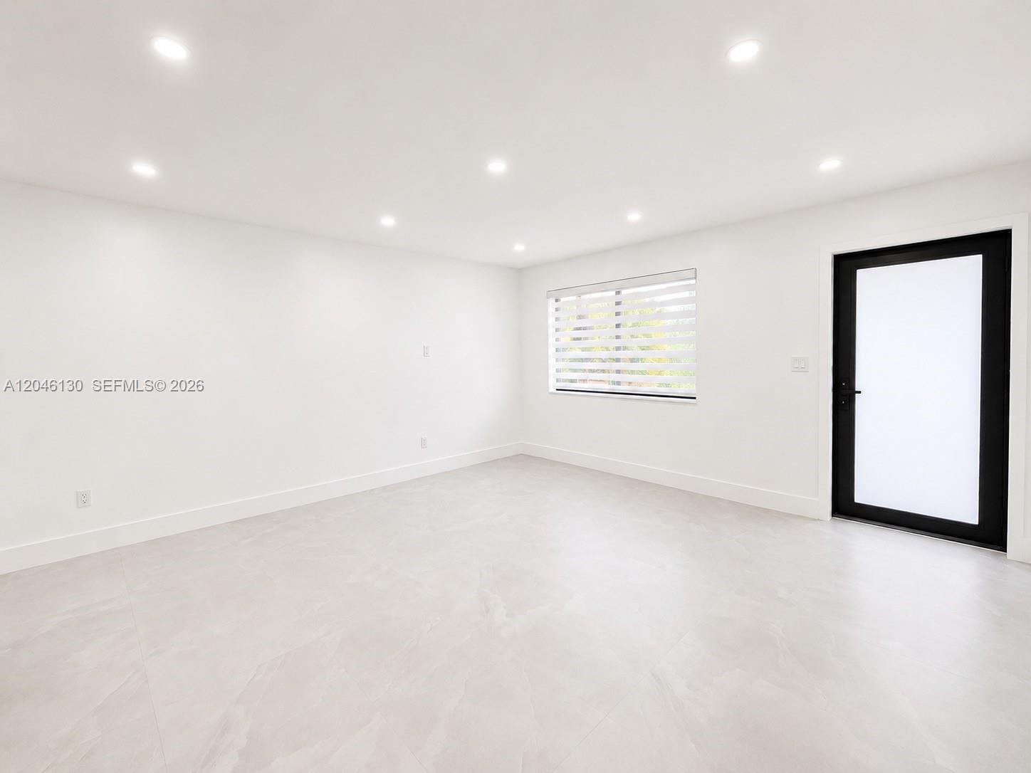 A minimalist room features white walls, light-colored tile flooring, recessed lighting, and a black-framed door — 1855 NW 93rd Ter # 2, Miami FL 33147, MIAMI, FL