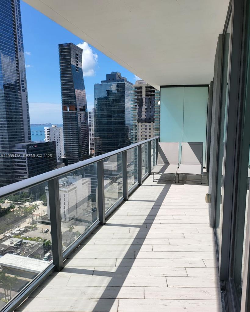 A high-rise balcony features light-colored tile flooring, glass railings, and two lounge chairs — 1300 S Miami Ave # 2501, Miami FL 33130, MIAMI, FL