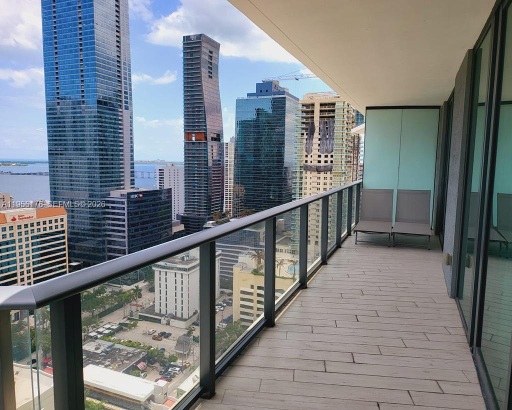 A balcony with wood-look flooring and two lounge chairs overlooks a dense urban skyline — 1300 S Miami Ave # 2501, Miami FL 33130, MIAMI, FL