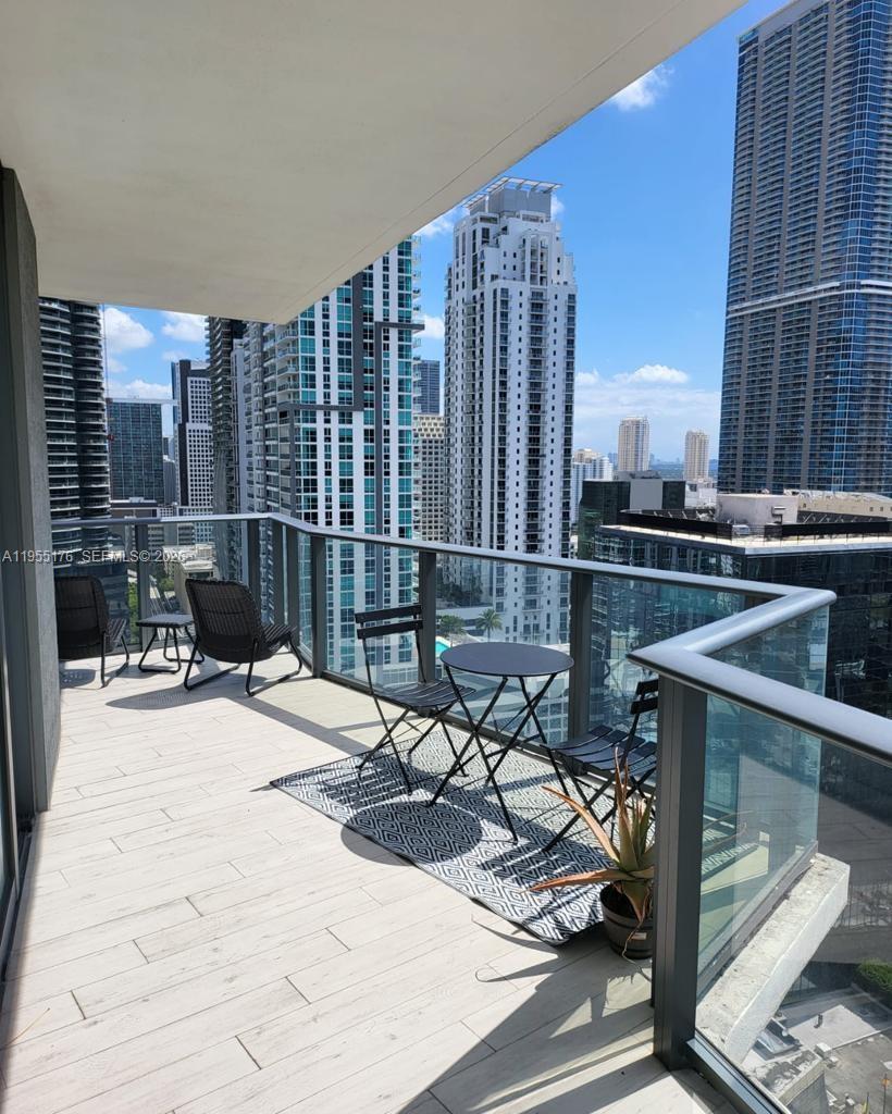 A high-rise balcony features light-colored tile flooring, outdoor furniture, and a view of city skyscrapers — 1300 S Miami Ave # 2501, Miami FL 33130, MIAMI, FL