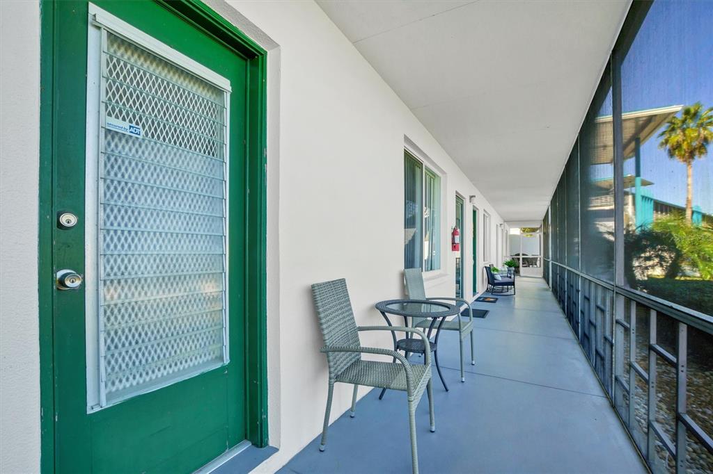 A long, covered outdoor balcony features a green door, patio furniture, and a screened enclosure — 1600 W LAKE PARKER DRIVE UNIT D5, LAKELAND, FL
