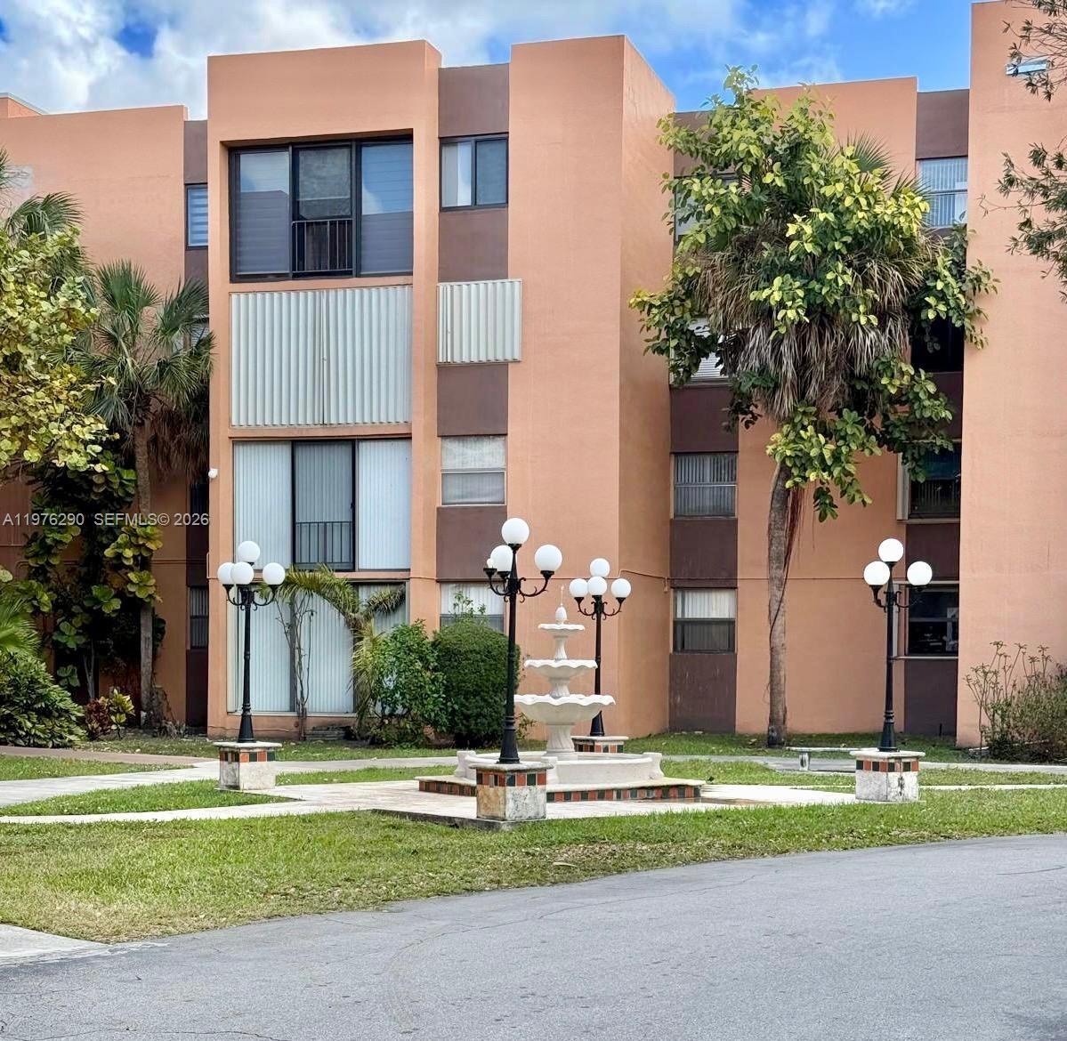 The exterior of a multi-story peach-colored apartment building features a central fountain and lampposts — 9400 WEST FLAGLER ST # 312, Miami FL 33174, MIAMI, FL