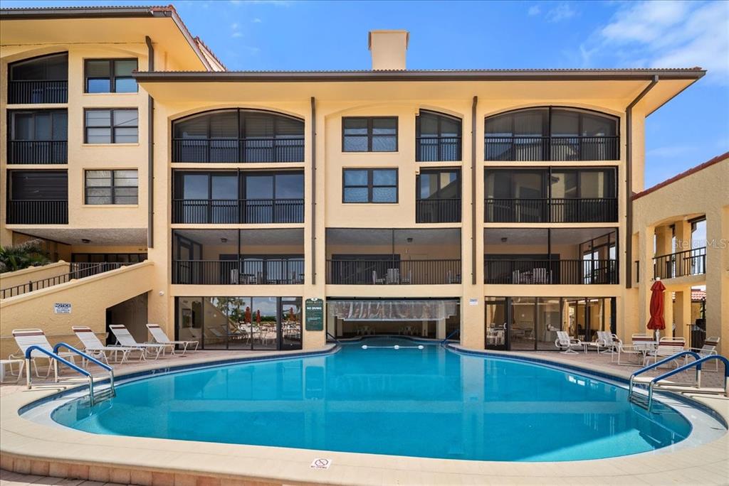 A multi-story yellow building features a swimming pool with lounge chairs on the patio — 8750 MIDNIGHT PASS ROAD UNIT 501, SARASOTA, FL