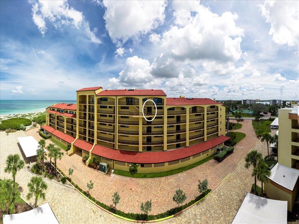An aerial view of a multi-story yellow apartment building with a red tile roof — 8750 MIDNIGHT PASS ROAD UNIT 501, SARASOTA, FL