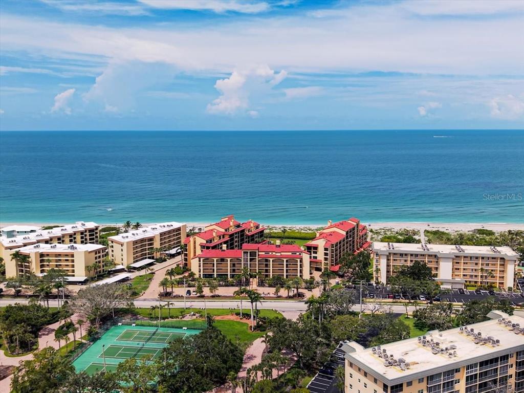 An aerial view shows beachfront apartment buildings, a tennis court, and a parking lot — 8750 MIDNIGHT PASS ROAD UNIT 501, SARASOTA, FL