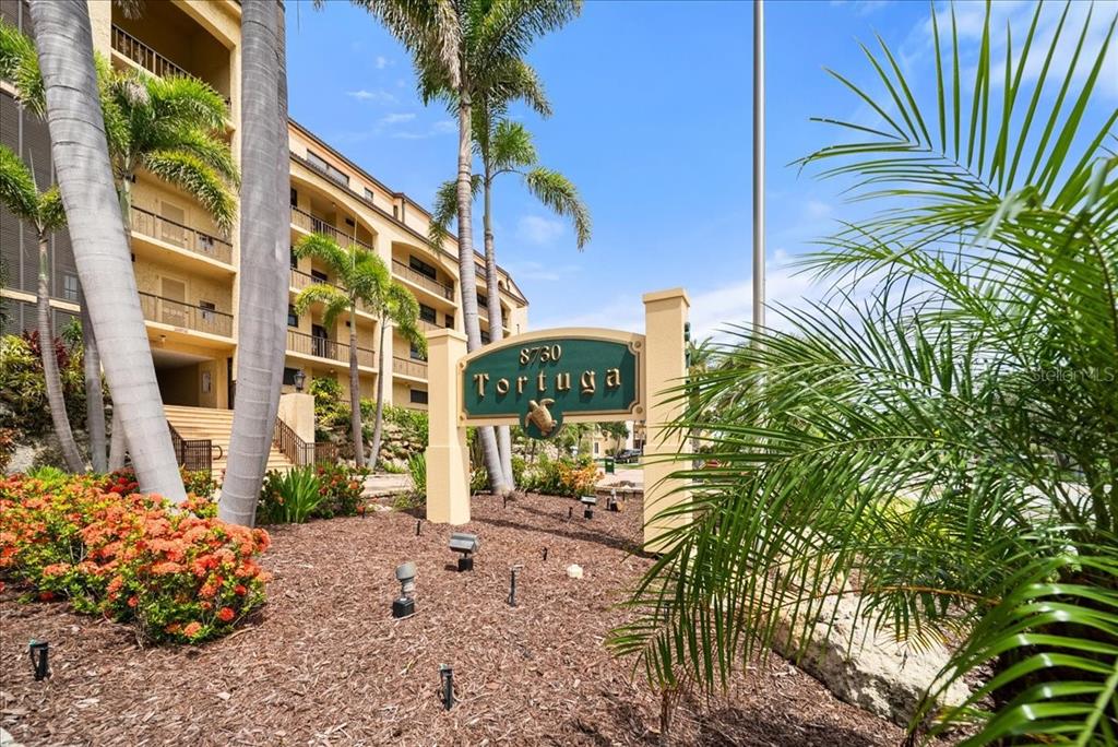 A sign for Tortuga stands in front of a multi-story apartment building with palm trees — 8750 MIDNIGHT PASS ROAD UNIT 501, SARASOTA, FL