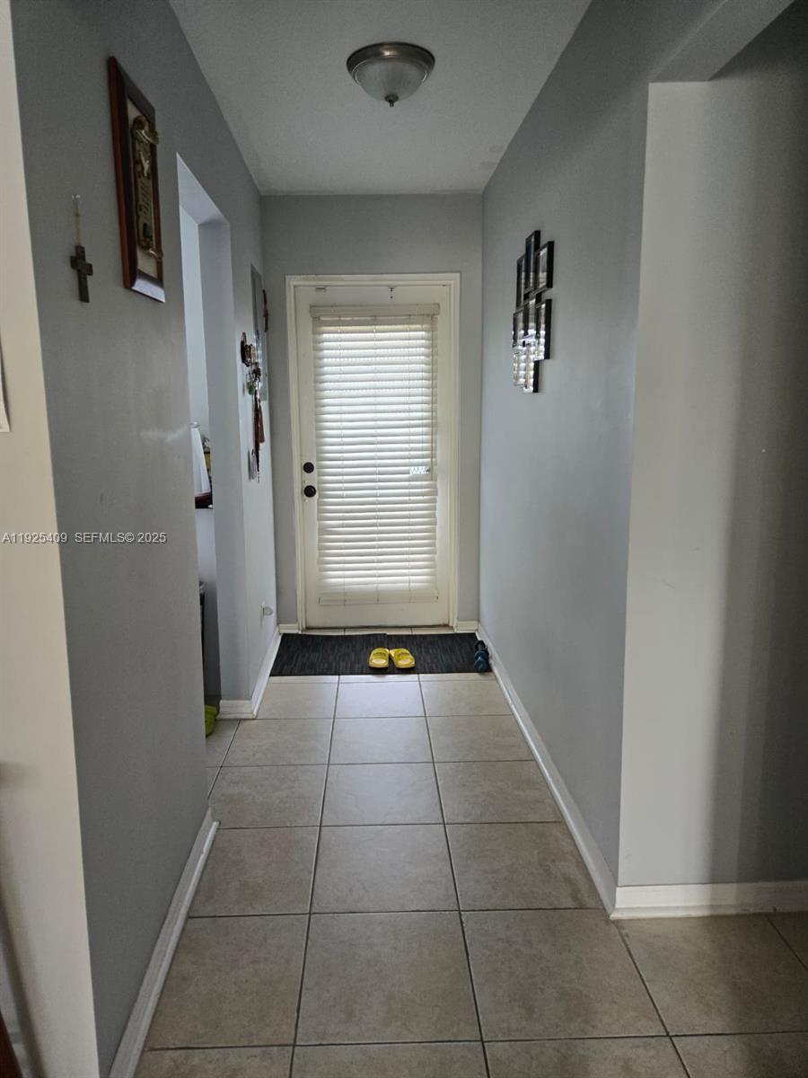 A hallway with light gray walls, tile flooring, and a door with blinds — 7837 Golf Cir Dr # 310, Margate FL 33063, MARGATE, FL