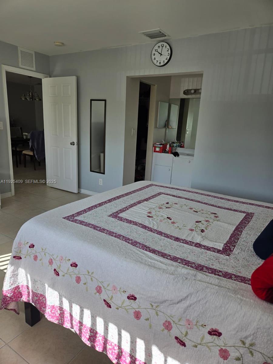 A bedroom features a bed with a floral quilt, a wall clock, and an open doorway — 7837 Golf Cir Dr # 310, Margate FL 33063, MARGATE, FL