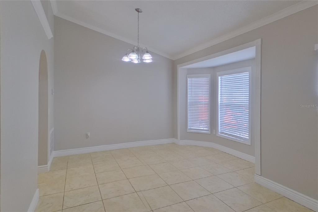 An empty dining room features light-colored tile flooring, a vaulted ceiling, and a bay window — 312 COLONY COURT, KISSIMMEE, FL