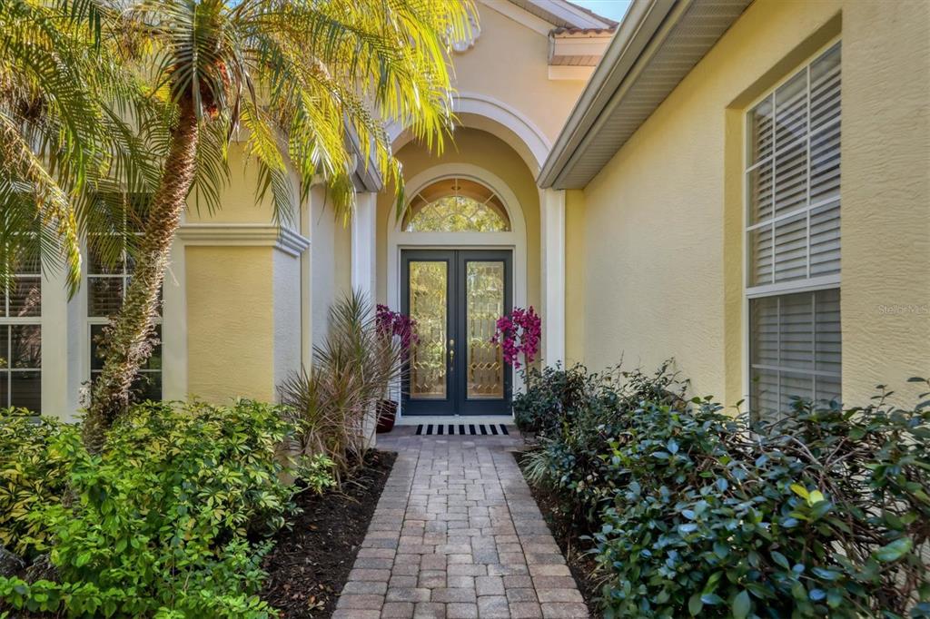 A stone walkway leads to a double front door under an arched entryway of a house — 8135 ABINGDON COURT, UNIVERSITY PARK, FL