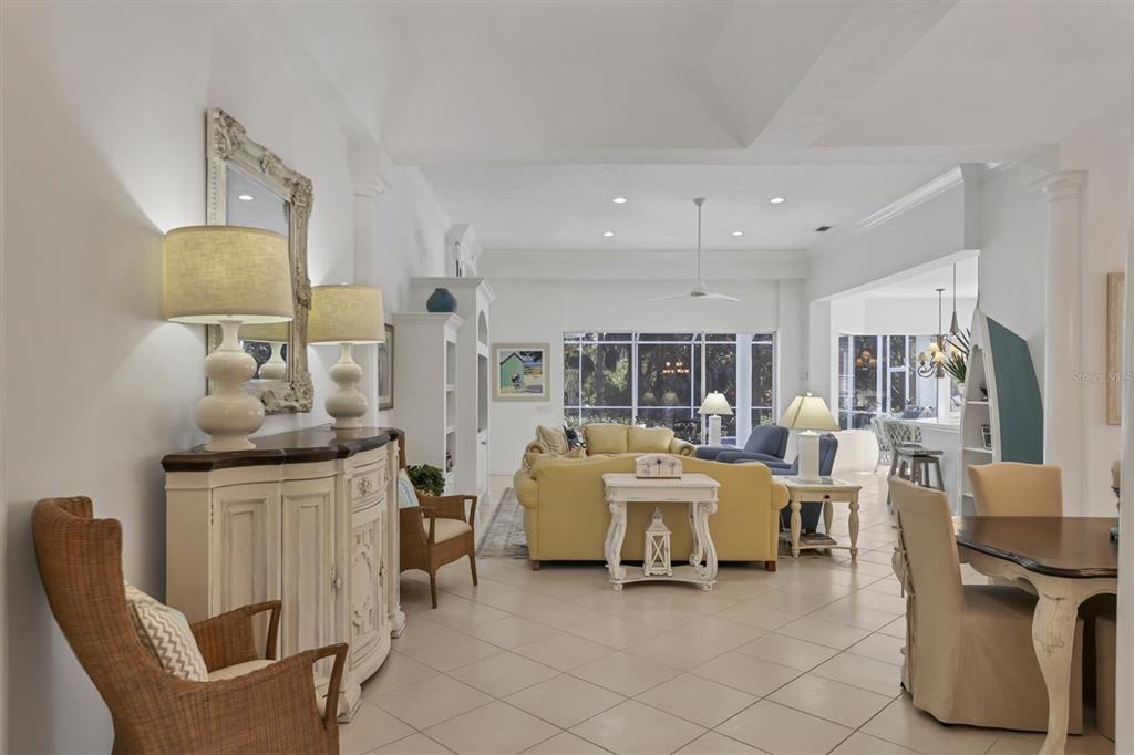 A bright, open-concept living and dining area features tile flooring, vaulted ceilings, and neutral decor — 8135 ABINGDON COURT, UNIVERSITY PARK, FL