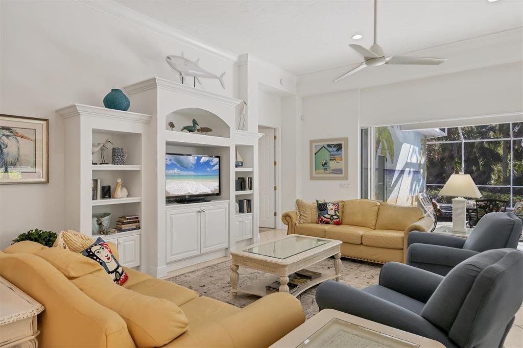 A living room features yellow sofas, blue armchairs, a white entertainment center, and large windows — 8135 ABINGDON COURT, UNIVERSITY PARK, FL