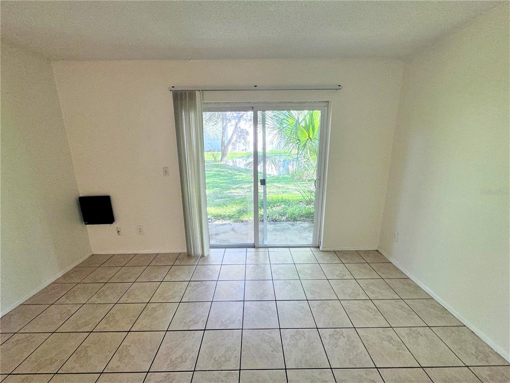 An empty room with beige tile flooring and a sliding glass door leading outside — 7177 E BANK DRIVE UNIT 102, TAMPA, FL
