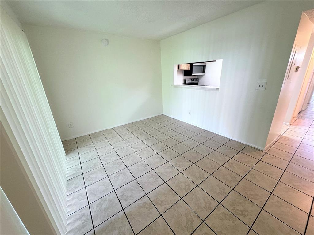 An empty dining area features beige tile flooring and a pass-through window to the kitchen — 7177 E BANK DRIVE UNIT 102, TAMPA, FL