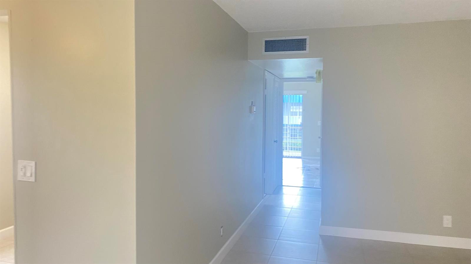 A hallway with light-colored walls and tile flooring leads toward a bright doorway — 177 Flanders D # 177, Delray Beach FL 33484, DELRAY BEACH, FL