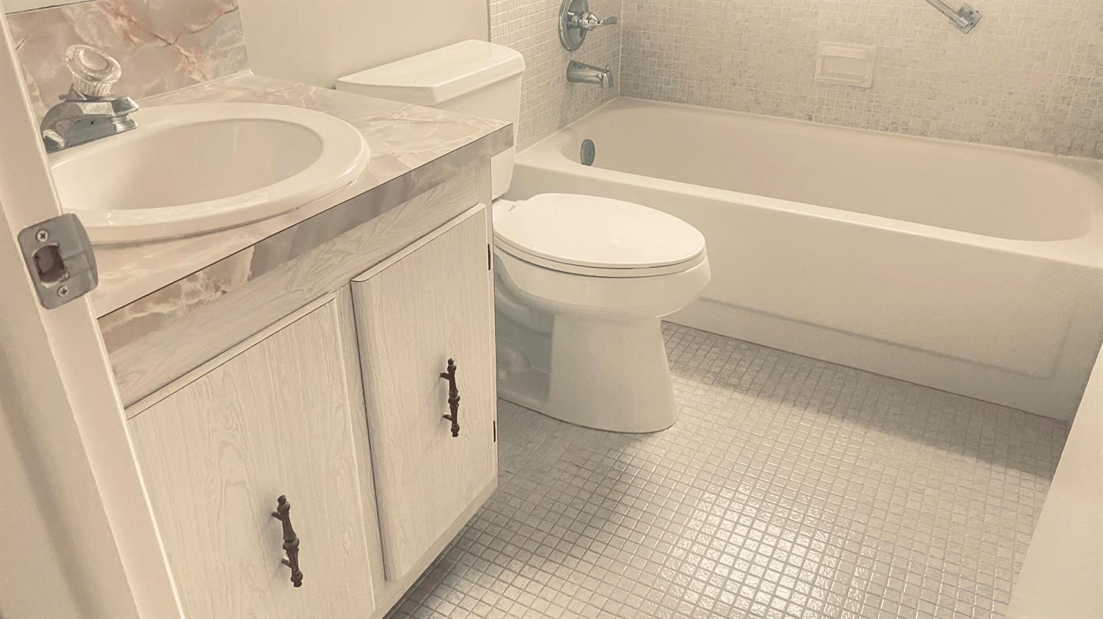 A bathroom features a white vanity with a marble-look countertop, toilet, and tiled bathtub surround — 177 Flanders D # 177, Delray Beach FL 33484, DELRAY BEACH, FL