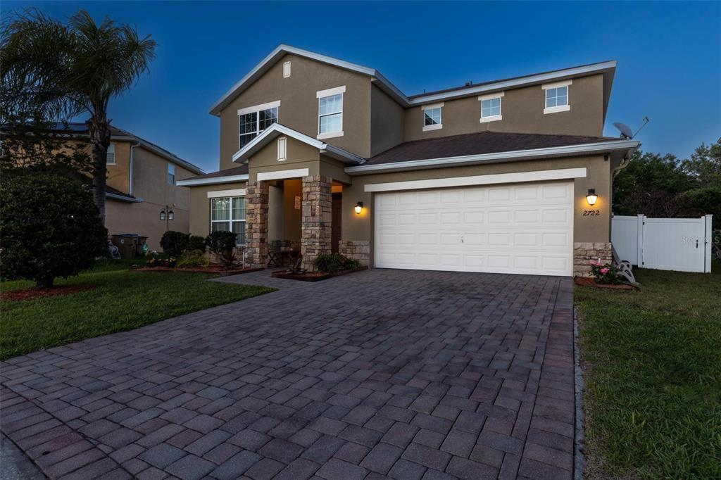 A two-story suburban house with a stone-accented entryway and a paved driveway at dusk — 2722 BIG TIMBER DRIVE, KISSIMMEE, FL