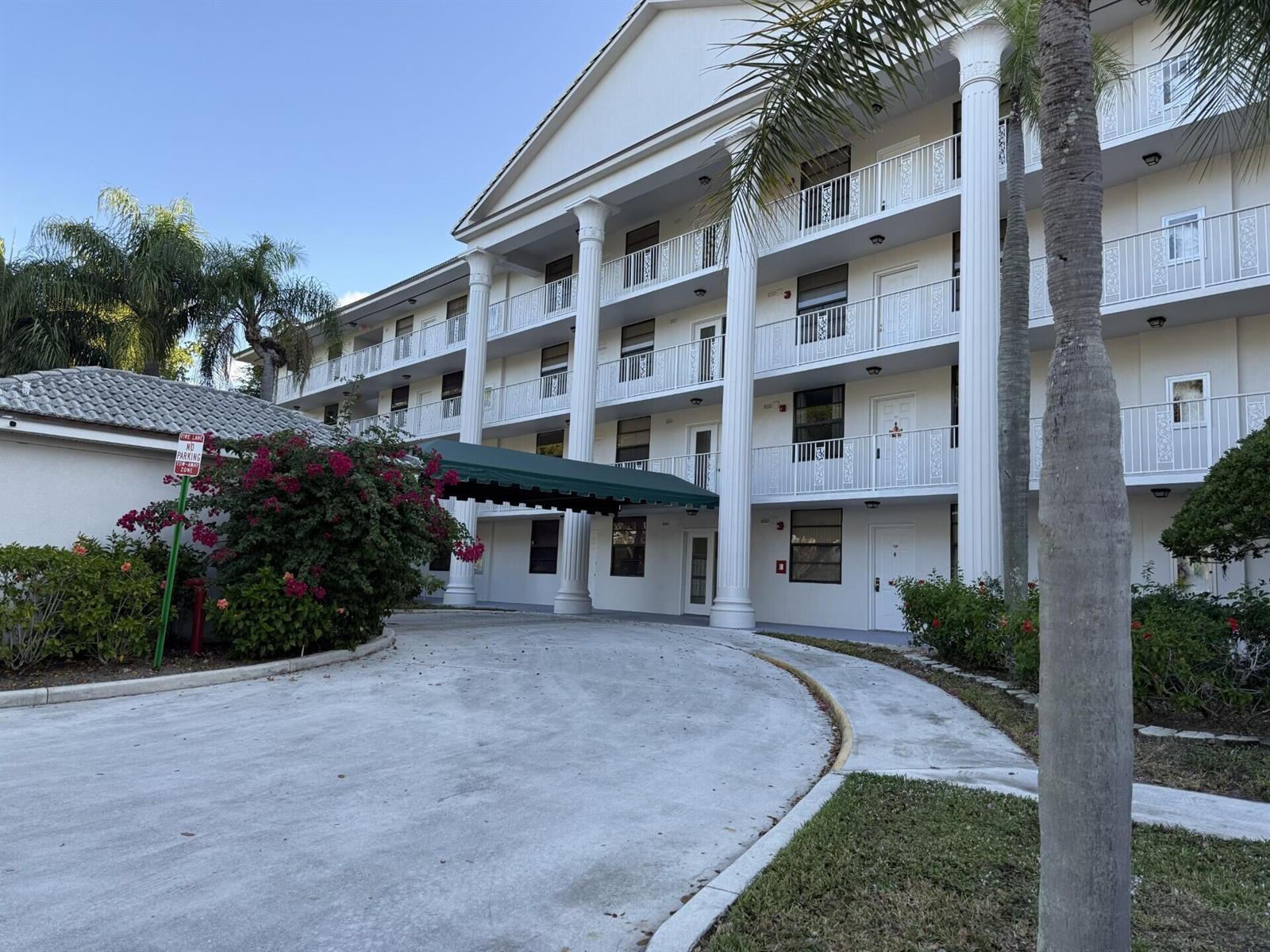 A multi-story building features white columns, a green awning, and balconies under a blue sky — 3710 Whitehall Drive # 401, West Palm Beach FL 33401, WEST PALM BEACH, FL
